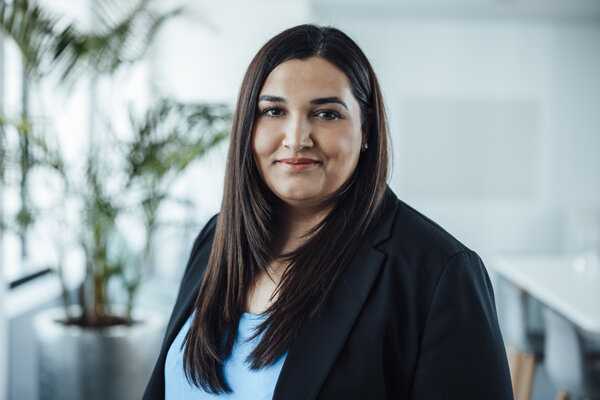 A portrait photograph of a woman standing sideways to the camera and wearing a black blazer.