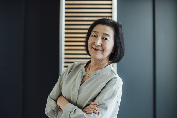 A portrait photograph of a woman in a blouse with her arms crossed in front of a wall.
