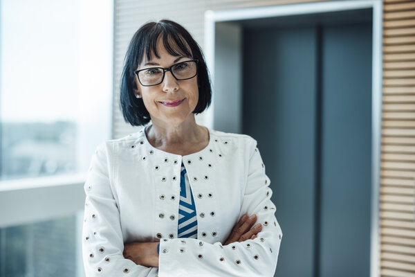 A portrait photograph of a woman standing between a window and a lift with her arms crossed.