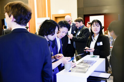 Several people in business attire are standing at an information stand with brochures.