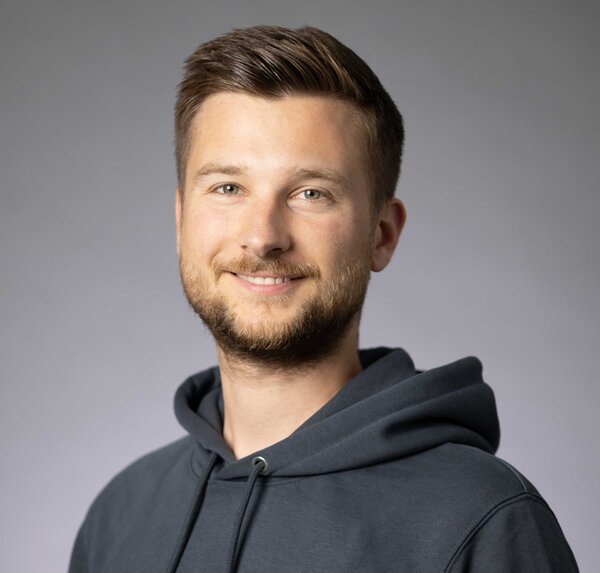 A portrait photograph of a young man wearing a hoodie and with styled brown-blond hair. 