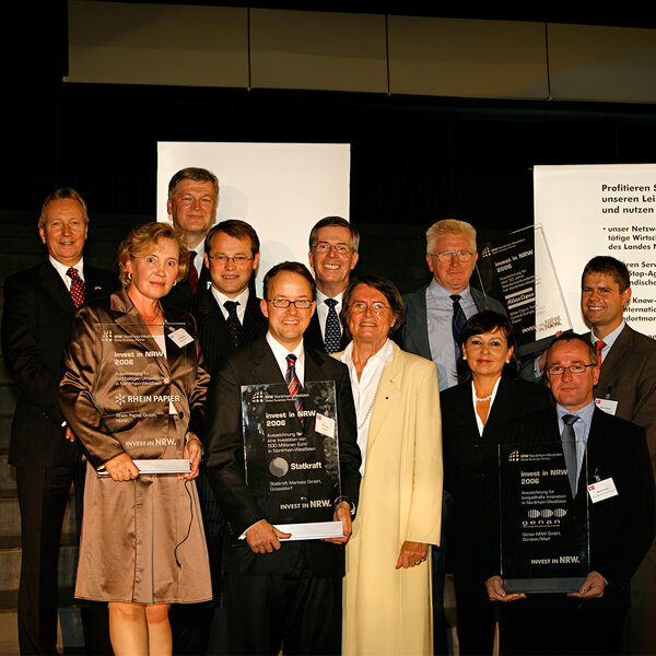 A large group of men and women in business attire. Several people are holding large, transparent trophies with various inscriptions. 