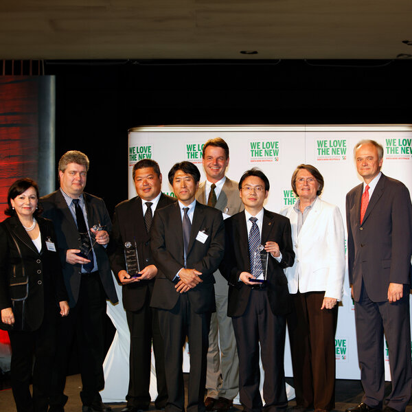 Eight people in business attire stand next to each other, some holding glass trophies in their hands.