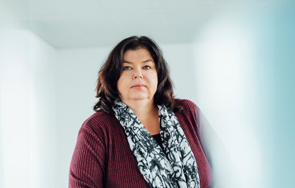 A portrait photograph of a woman sitting behind an office desk wearing a black and white patterned scarf.