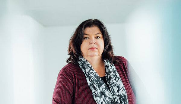 A portrait photograph of a woman sitting behind an office desk wearing a black and white patterned scarf.