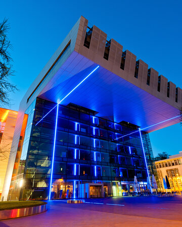 Modern building with blue lighting and glass façade at night, surrounded by trees and street lights.