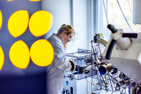 Eine Frau im weißen Laborkittel arbeitet mit Schutzhandschuhen an einem Laborgerät.