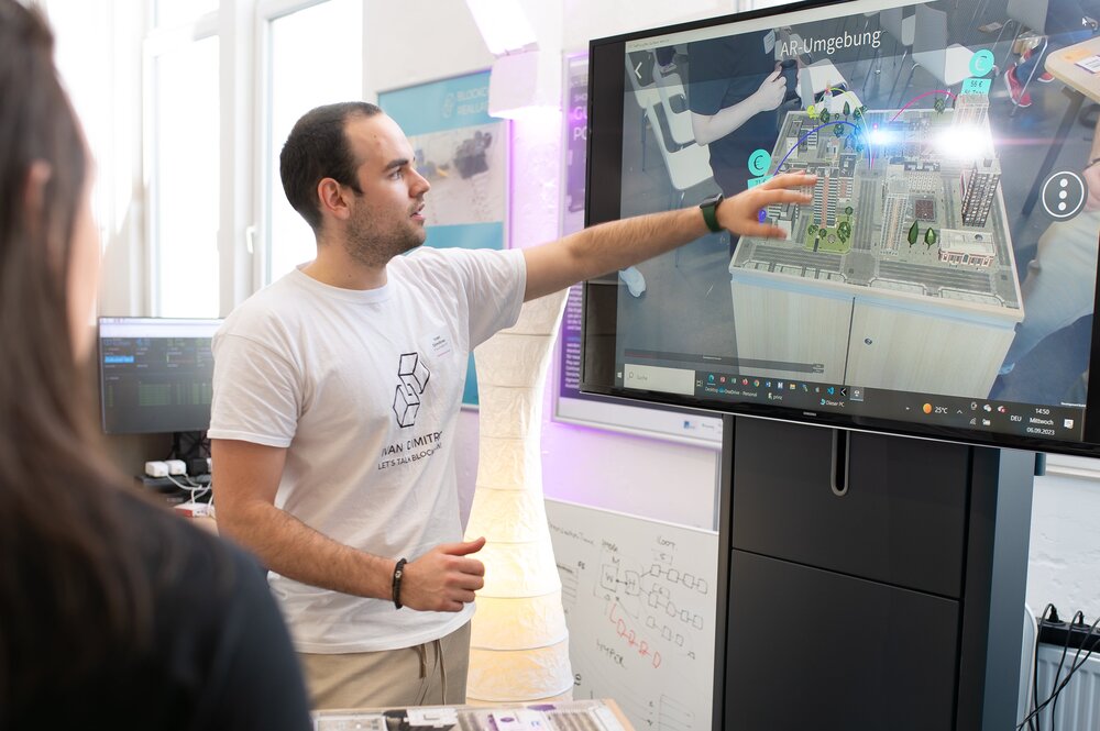 Ein Mann präsentiert an einem Bildschirm eine Augmented Reality-Umgebung mit einem digitalen Stadtmodell im Mittelpunkt.